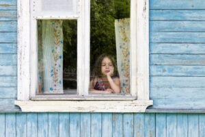 pessoa triste olhando pela janela da casa